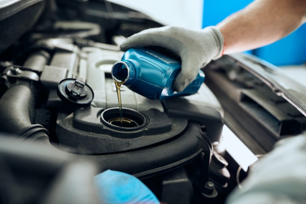 Close- up of mechanic pouring motor oil while doing car maintenance at auto repair shop.