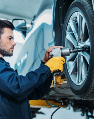 Automechanic unscrewing tire bolts on a lifted up car at a repair shop.