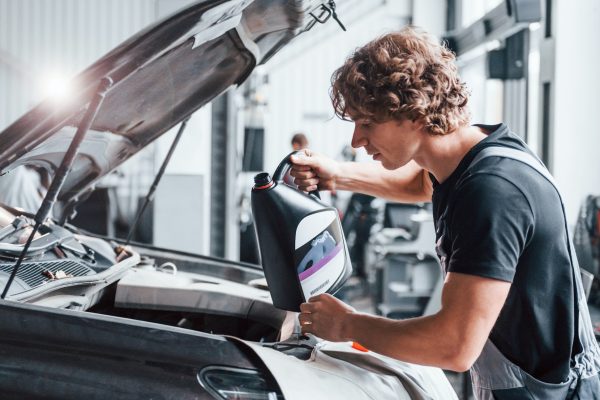 Changing oil. Adult man in grey colored uniform works in the automobile salon